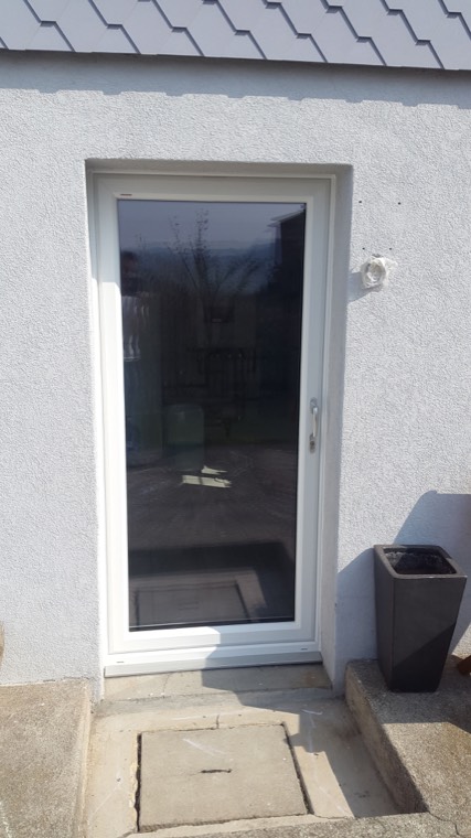 Weisse Tür mit grossem Glasfeld an grauer Fassade